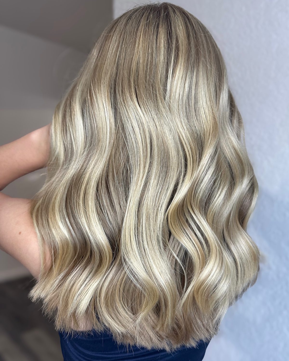 Back view of long, softly waved hair with bright, dimensional blonde highlights and a blended root